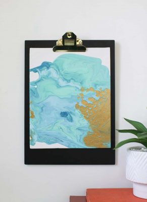 diy paint pour canvas art in aqua colors with gold and gold accents on a clipboard