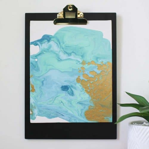 diy paint pour canvas art in aqua colors with gold and gold accents on a clipboard