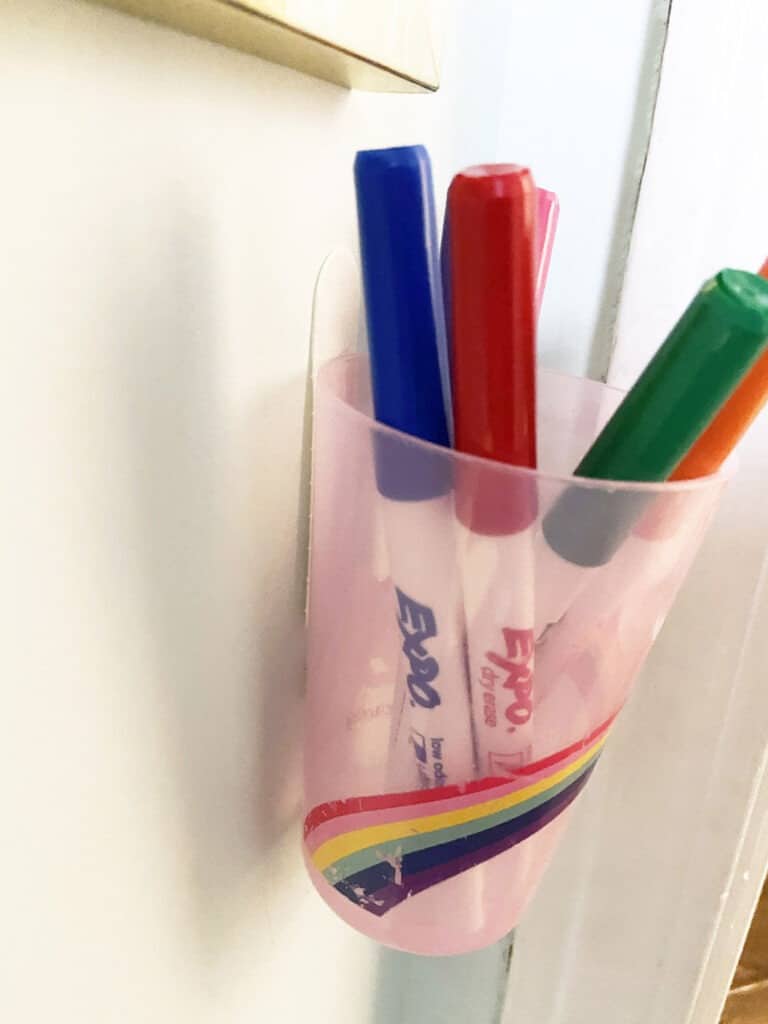 Use a command strip to attach a cup to the wall to hold dry erase markers