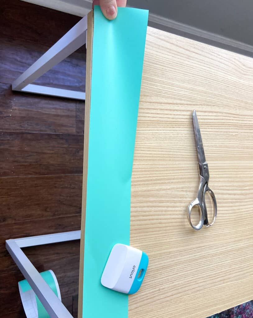 applying turquoise mint vinyl to a table top design with a burnishing tool and fingers