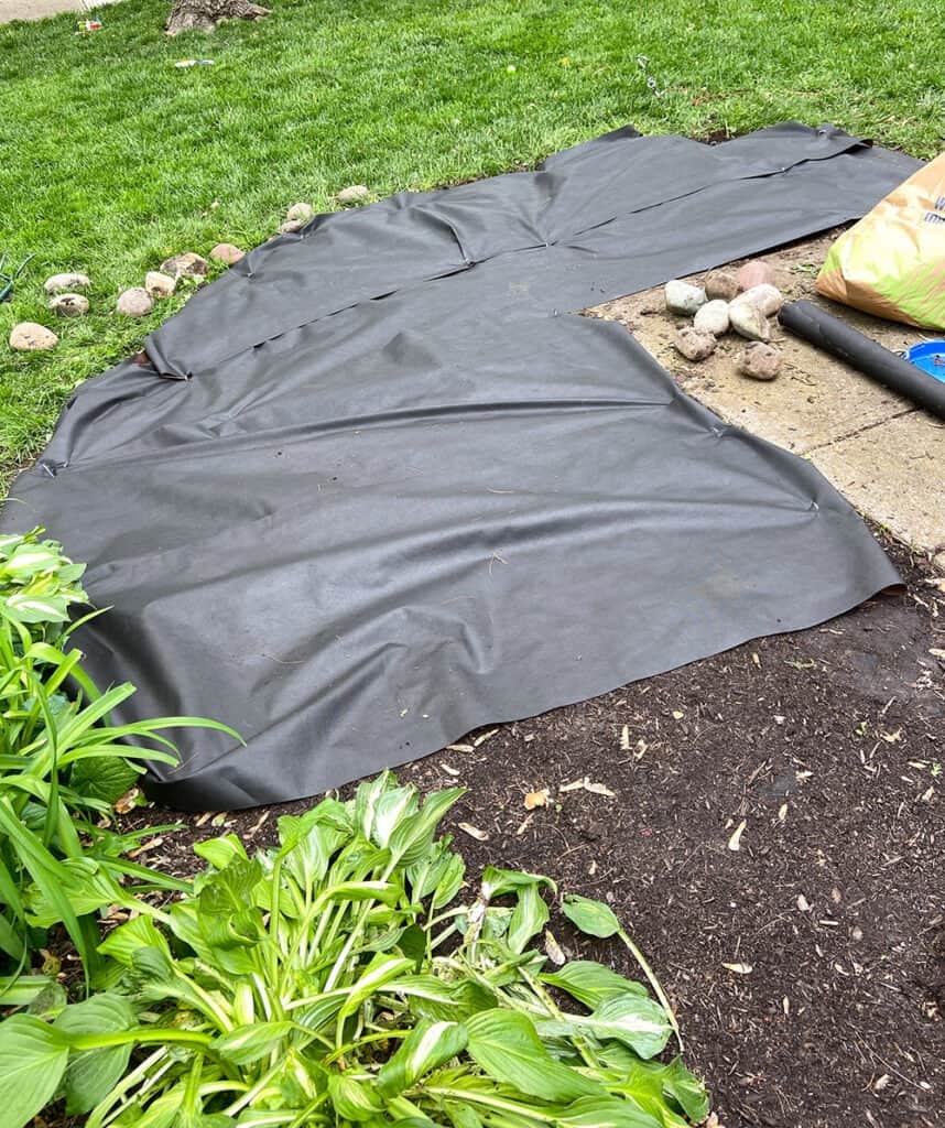 tearing out overgrown weeds from landscaping, laying weed mat, and mulching