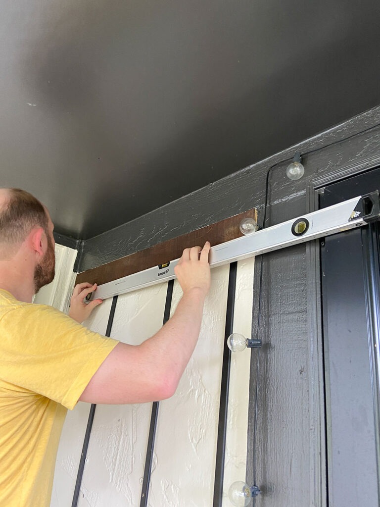 Installing wood slat to wall using a level, shim, and drill