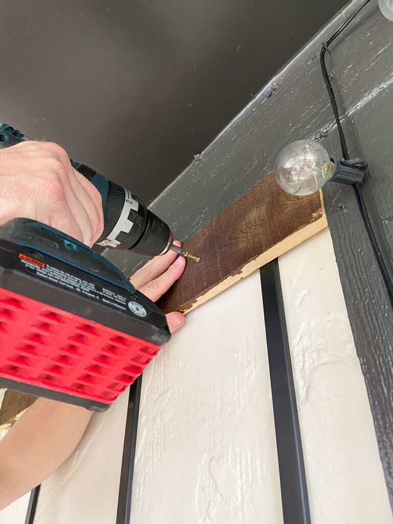 Installing wood slat to wall using a level, shim, and drill