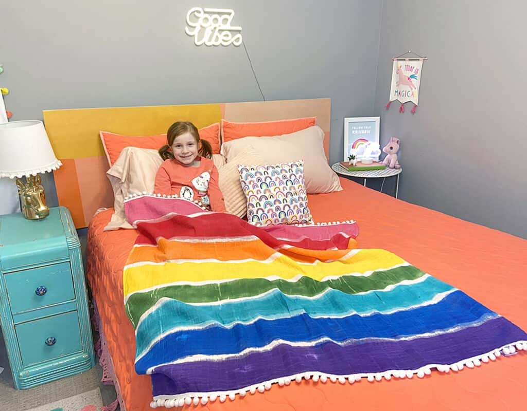 Rainbow blanket tutorial – Learn just how easy it is to make this cute and colorful decorative throw with festive pom pons.