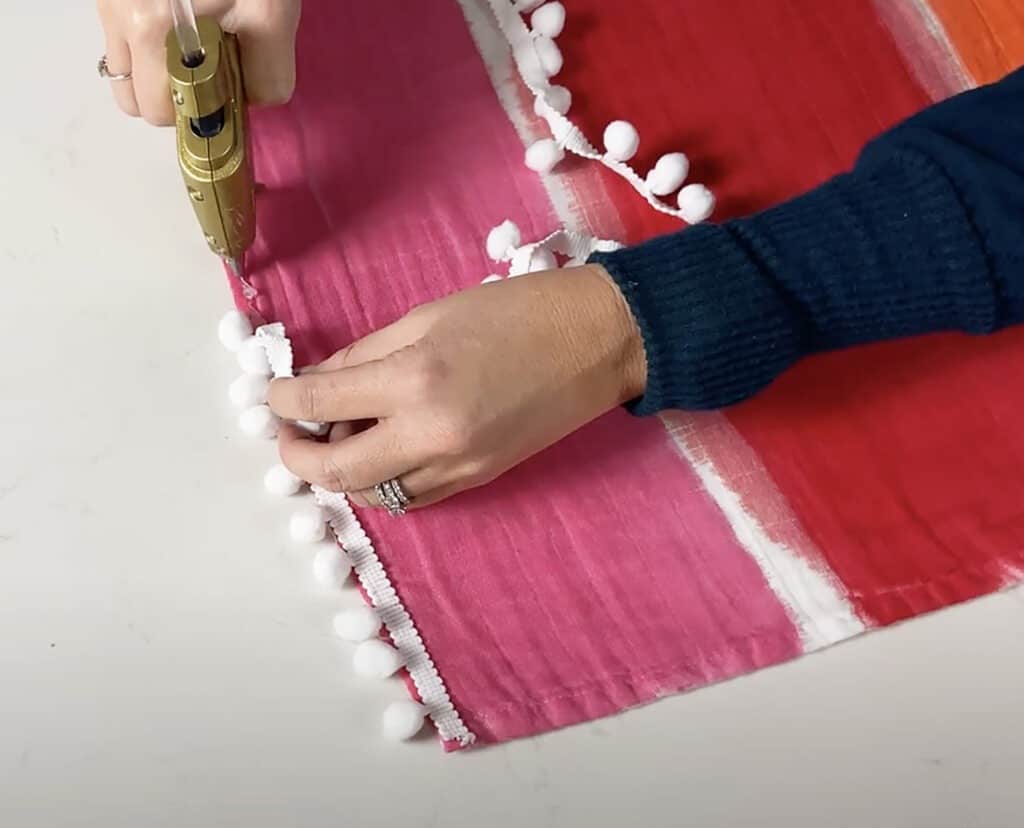 hot gluing pom pon trim ribbon to the blanket