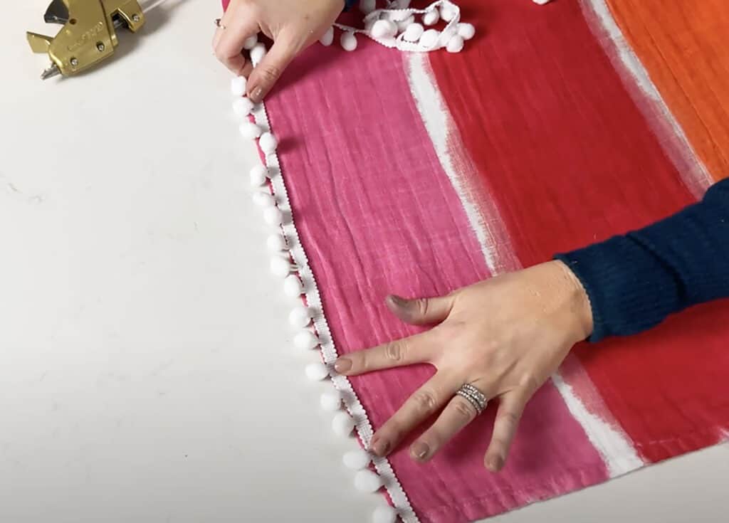 hot gluing pom pon trim ribbon to the blanket