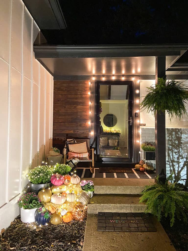 fall front porch at night with lots of pumpkins and fairy lights