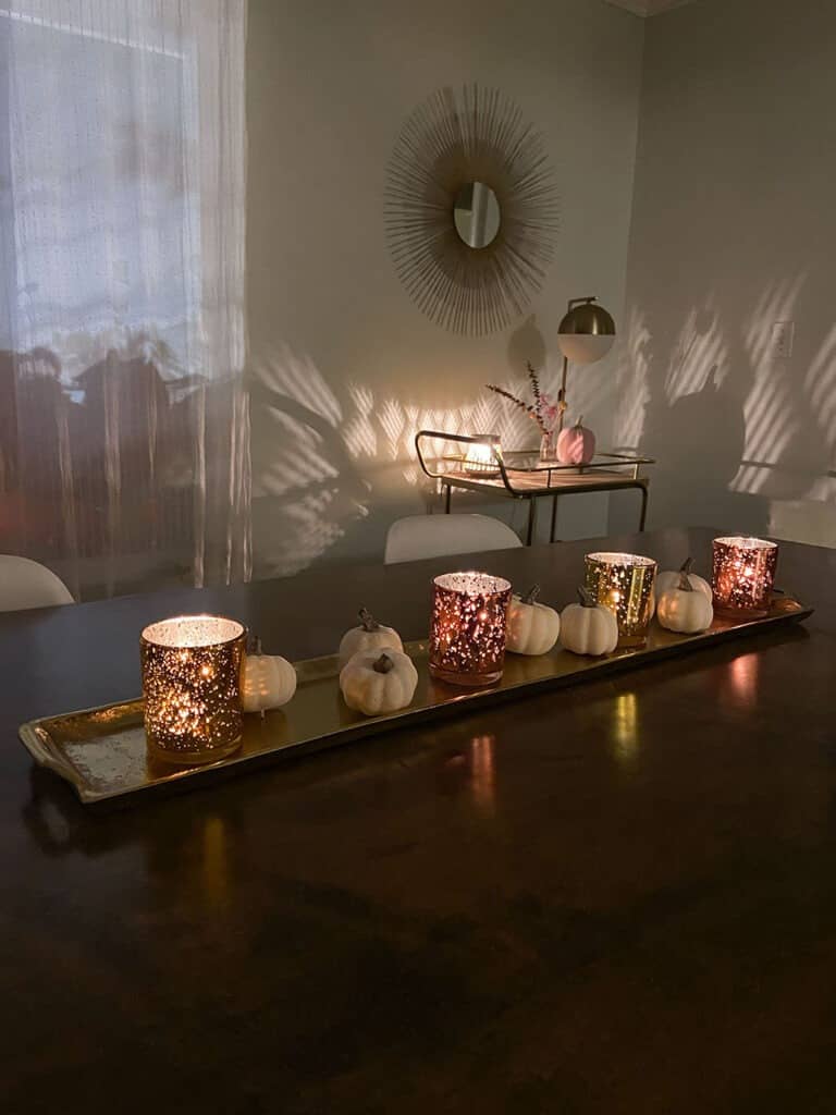 Dining room table with a gold tray, candles, faux blush pumpkins and a decorated bar cart in the background