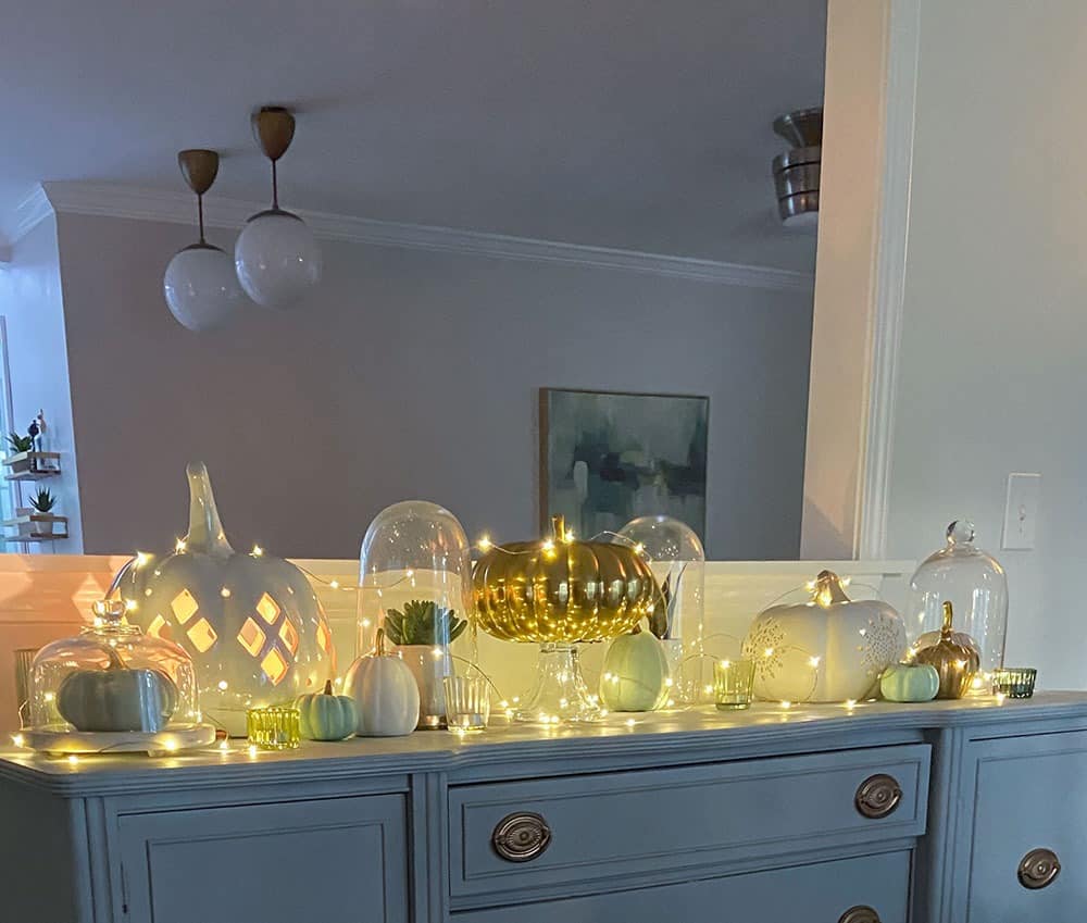 faux pumpkins, plants, glass cloches, candles, and fairy lights on a vintage cabinet top - easy fall decorating ideas!