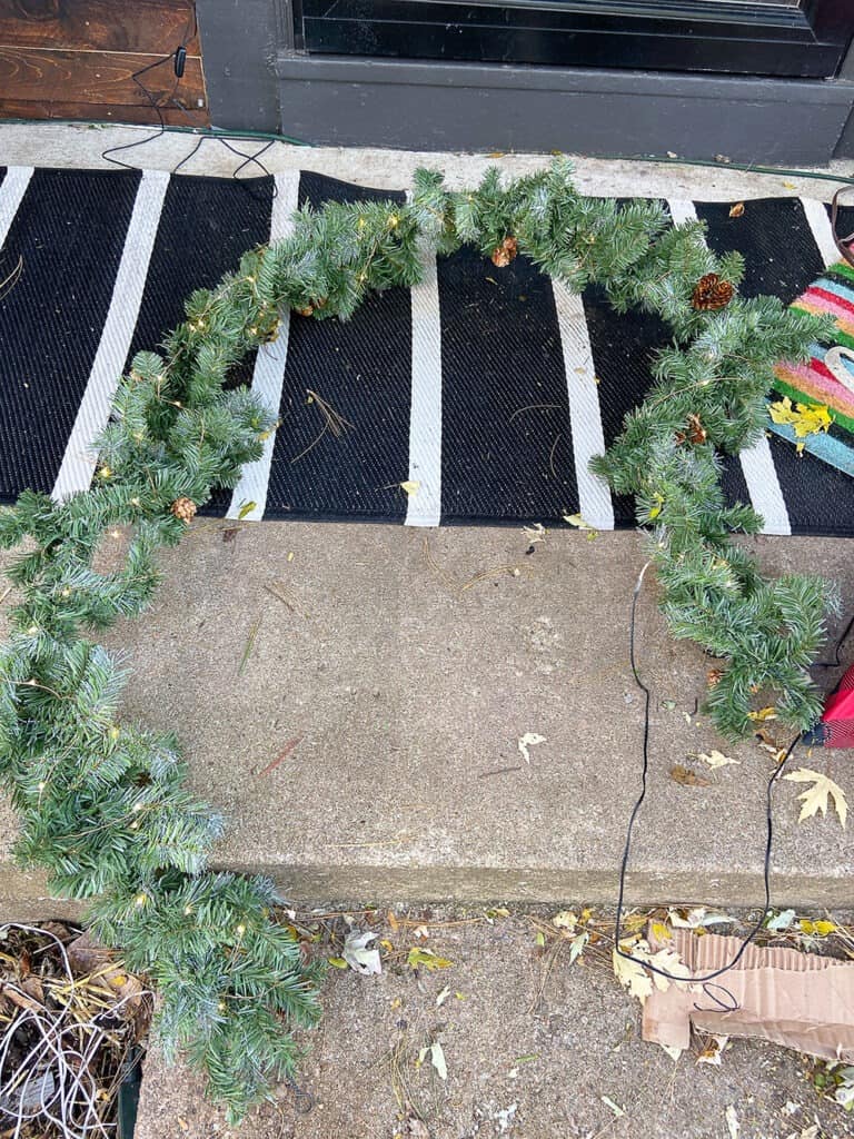 front porch holiday decor in process shot - adding fairy lights ot green garland