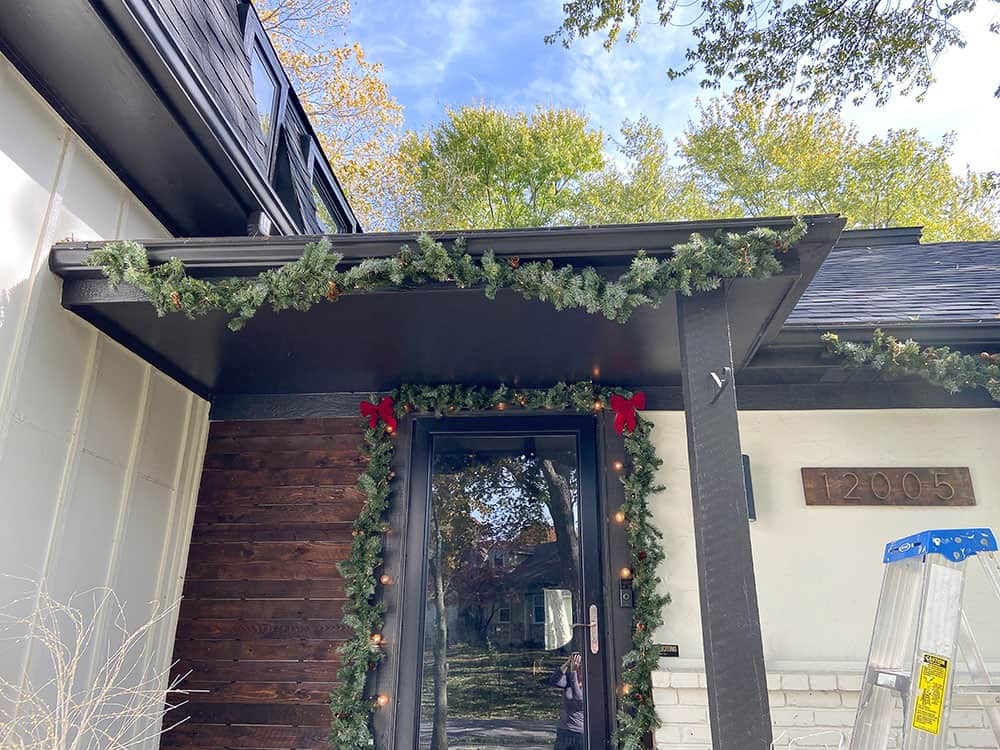 adding fairy lights and garland to gutters on porch and front of house