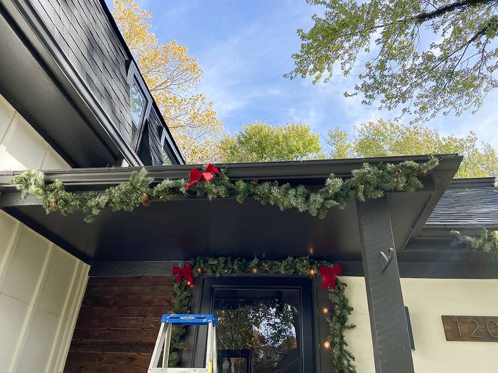 adding fairy lights and garland to gutters on porch and front of house