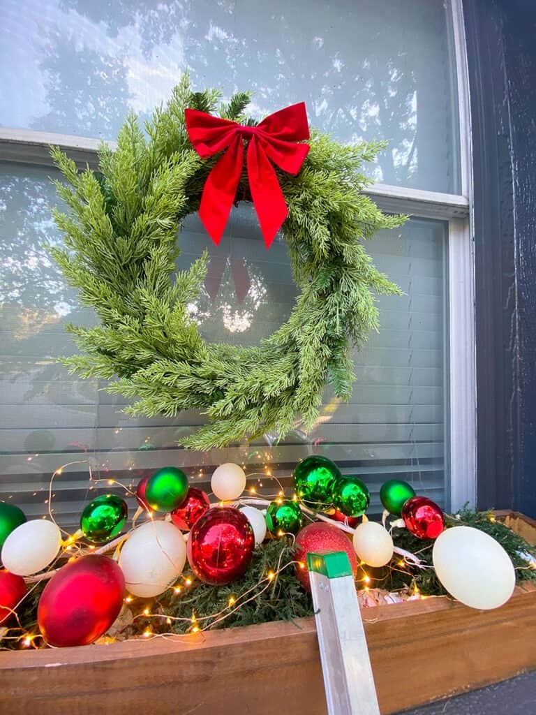 outdoor holiday window box decor using ornament garland and a classic wreath