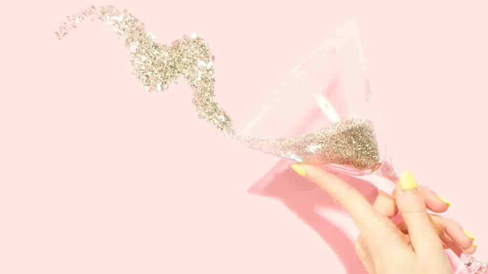 January 2022 pink background with hand holding champagne glass of gold glitter