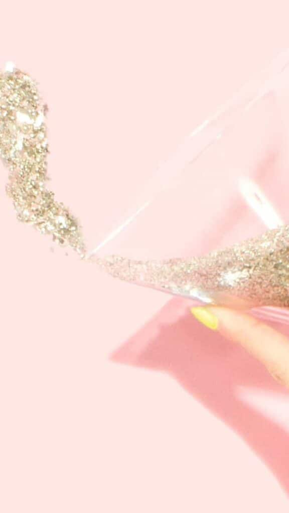 January 2022 pink background with hand holding champagne glass of gold glitter