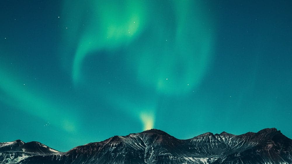 electric green and yellow northern lights in Iceland mountains