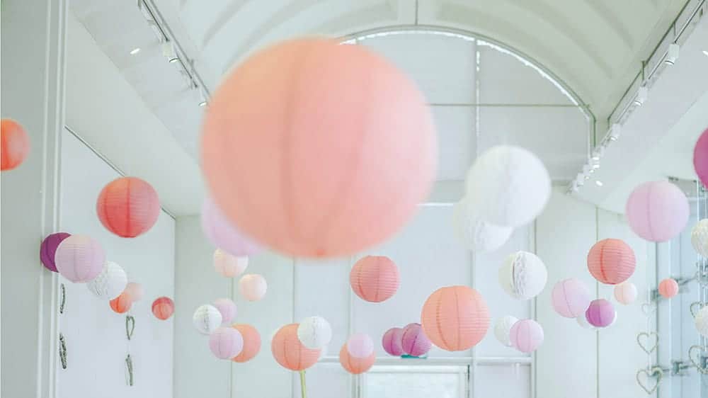 pink, purple, peach, white, and coral round paper lanterns hanging in a white room