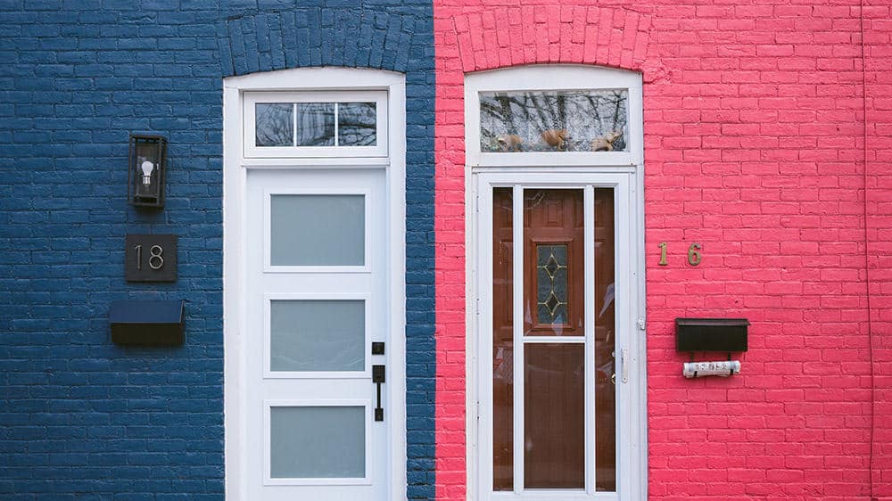 blue painted brick building with white door next to a pink painted brick building with white door london flat