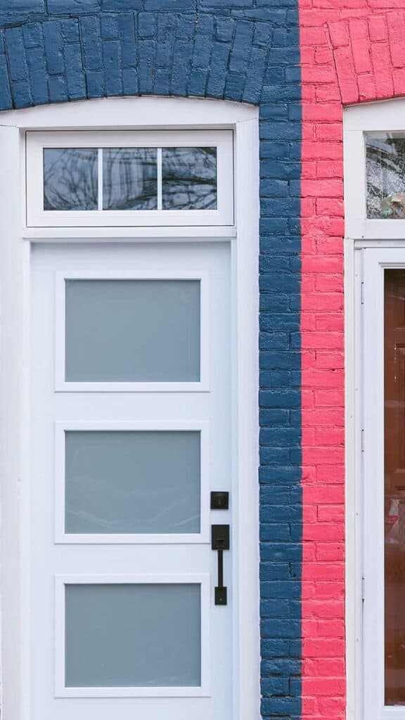 blue painted brick building with white door next to a pink painted brick building with white door london flat