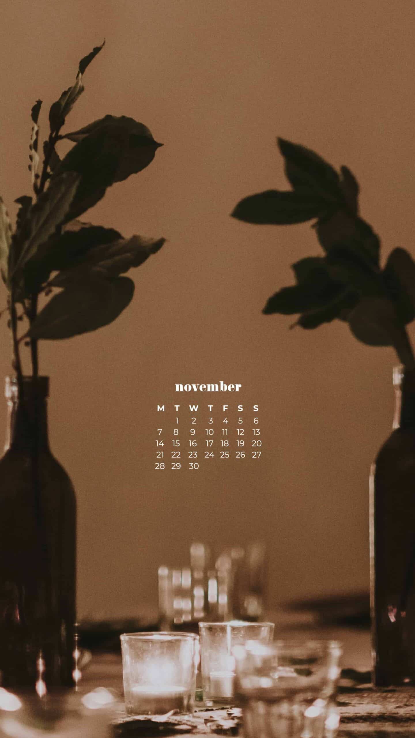 dim thanksgiving shot of a beautiful but simple table scape. tall bottles with greenery in them and clear glassware. Blurry background November 2022 wallpapers – FREE calendars in Sunday & Monday starts + no-calendar designs. 59 beautiful options for desktop & smart phones!