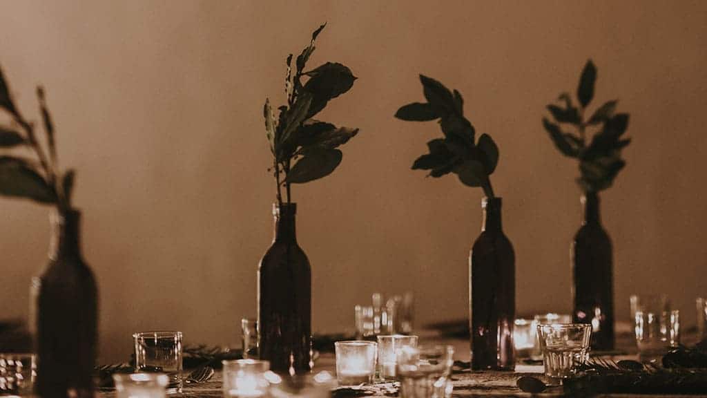 dim thanksgiving shot of a beautiful but simple table scape. tall bottles with greenery in them and clear glassware. Blurry background November 2022 wallpapers – FREE calendars in Sunday & Monday starts + no-calendar designs. 59 beautiful options for desktop & smart phones!