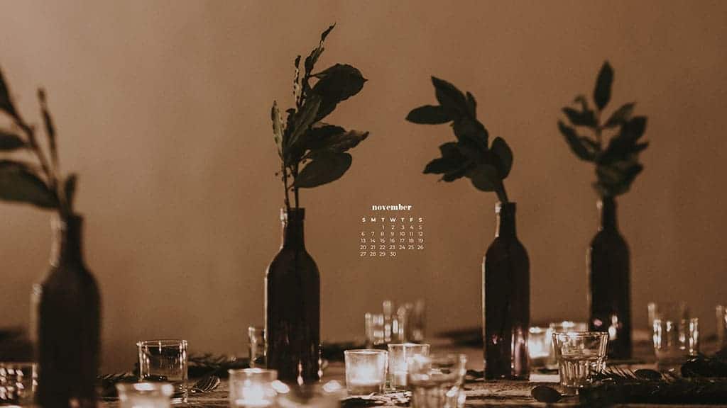 dim thanksgiving shot of a beautiful but simple table scape. tall bottles with greenery in them and clear glassware. Blurry background November 2022 wallpapers – FREE calendars in Sunday & Monday starts + no-calendar designs. 59 beautiful options for desktop & smart phones!