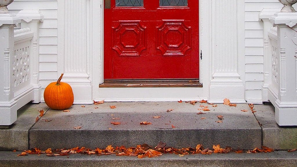 white house red door with leaves and a fall pumpkin 