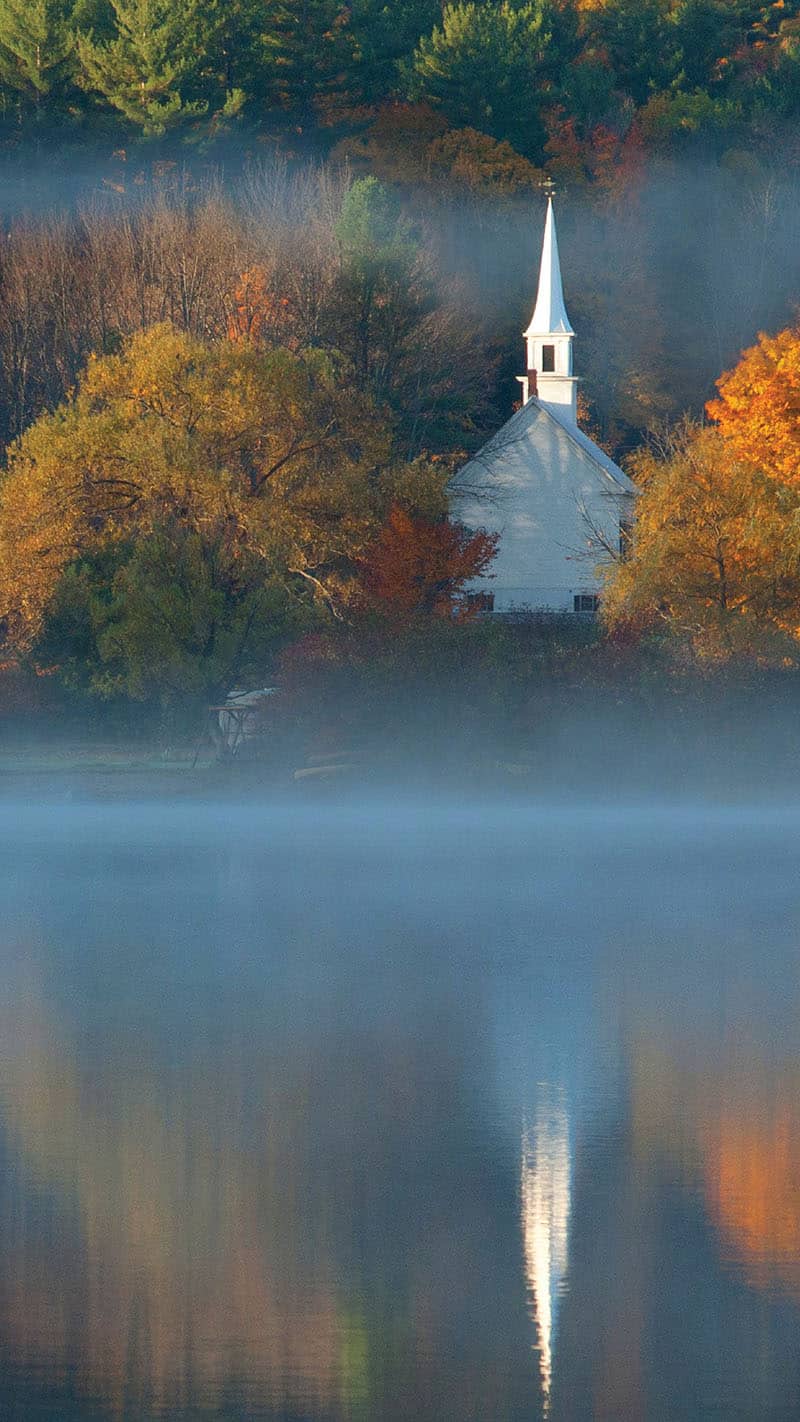 all trees and an old white church with lake reflection