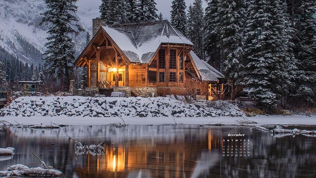 beautiful snow covered cabin on a lake surrounded by pine trees